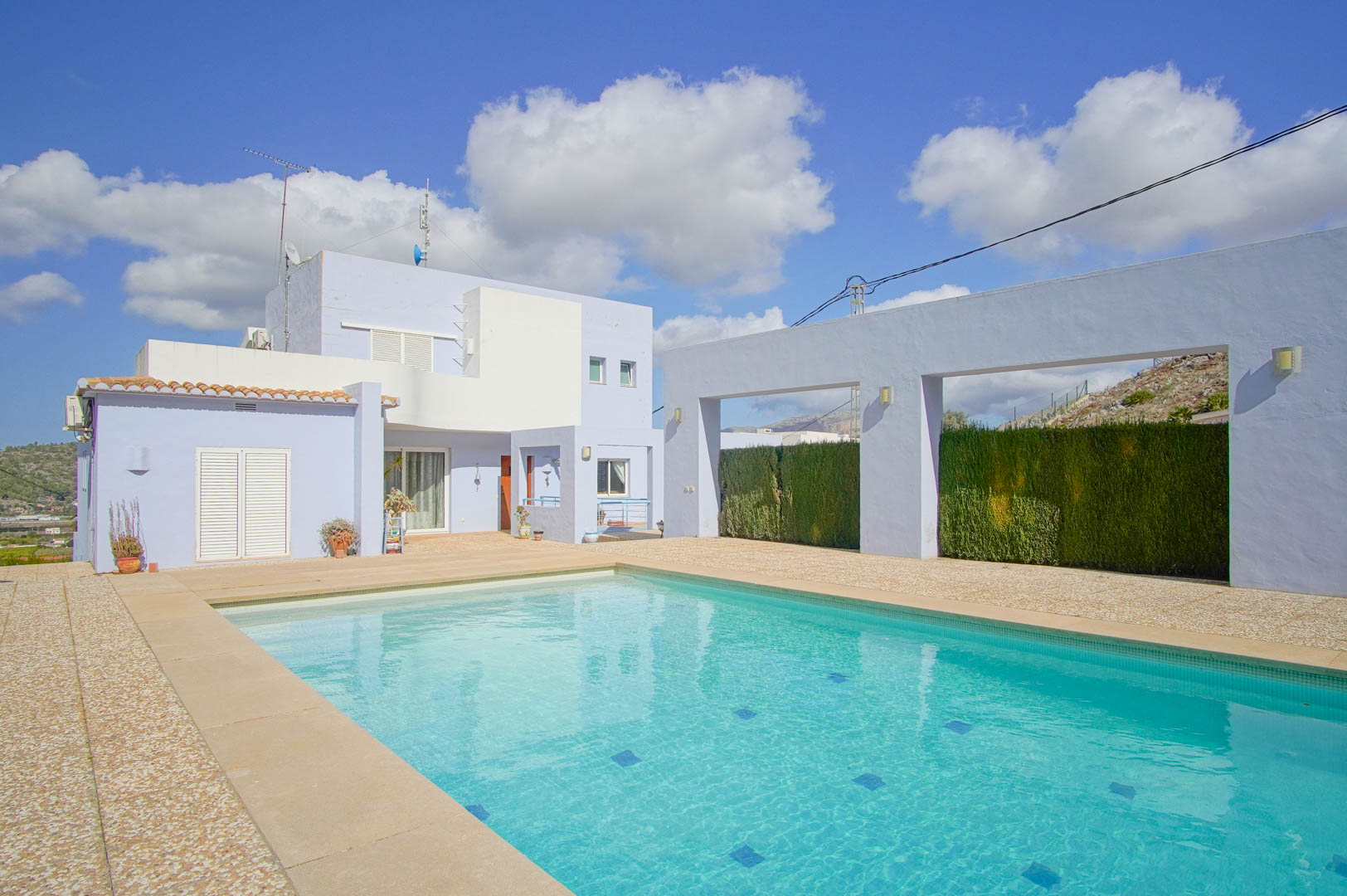 Piscine rectangulaire entourée d'une terrasse en pierre, mettant en valeur la façade moderne bleue et blanche de la villa et ses murs architecturaux.