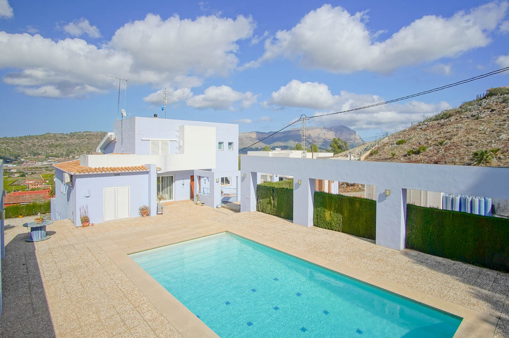 Piscine rectangulaire et terrasse en pierre devant la façade lavande de la villa, offrant une vue dégagée sur les montagnes environnantes.
