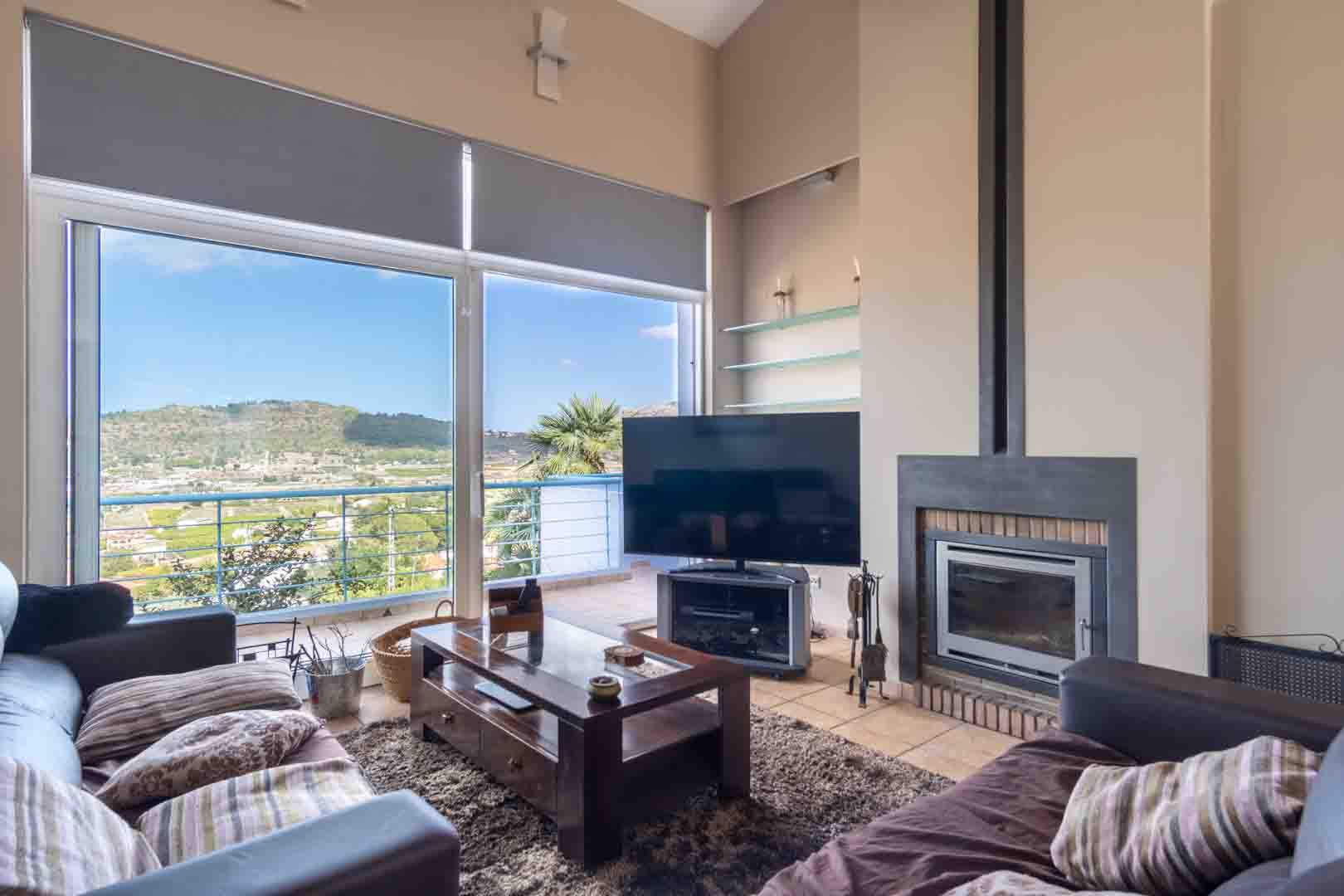 Salon lumineux avec cheminée encastrée, sol en grès et grandes baies vitrées offrant une vue panoramique sur la vallée et les montagnes environnantes.