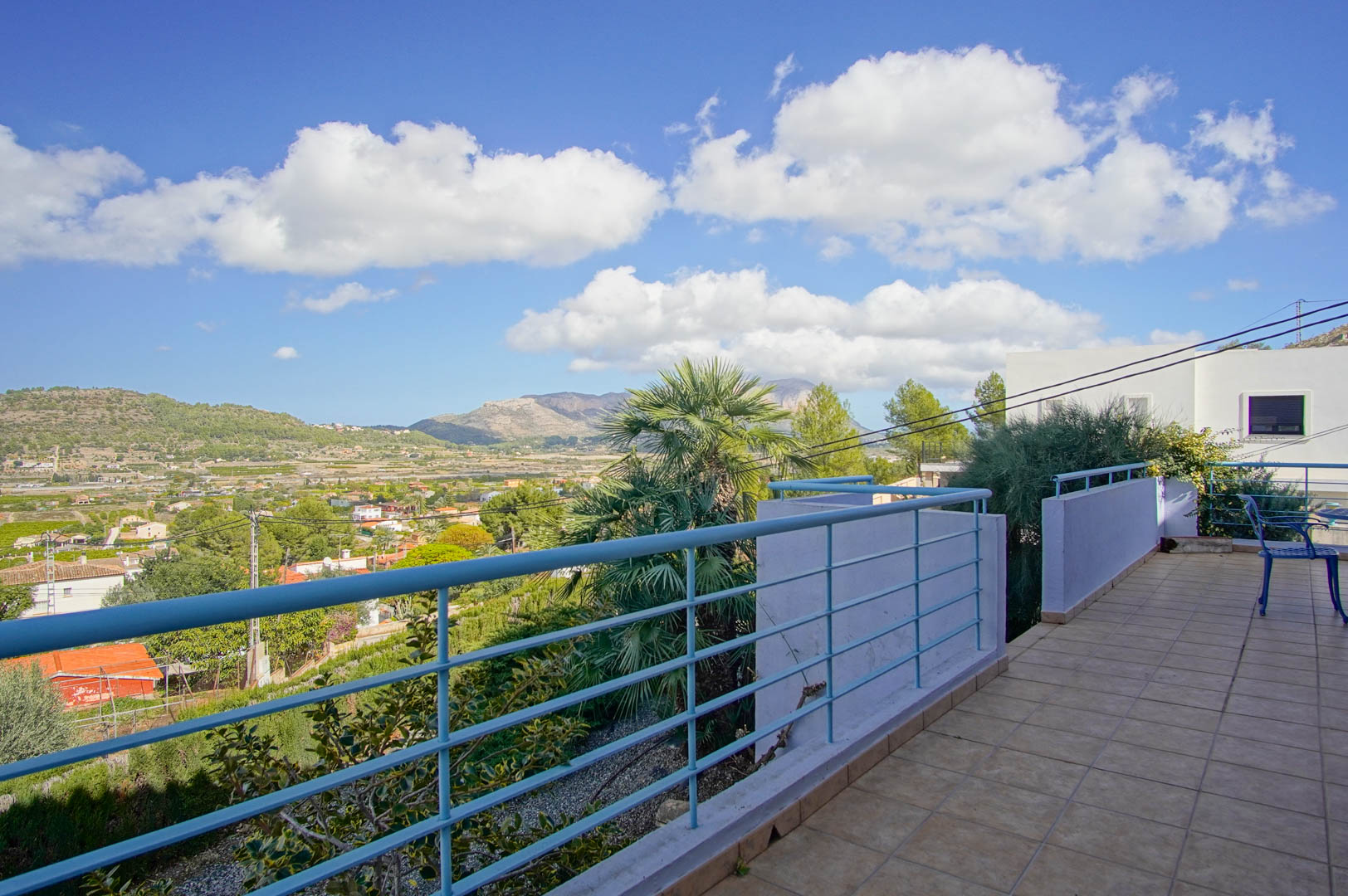 Terrasse supérieure avec carrelage et garde-corps bleu, offrant une vue panoramique sur la vallée de Pedreguer et les montagnes méditerranéennes.
