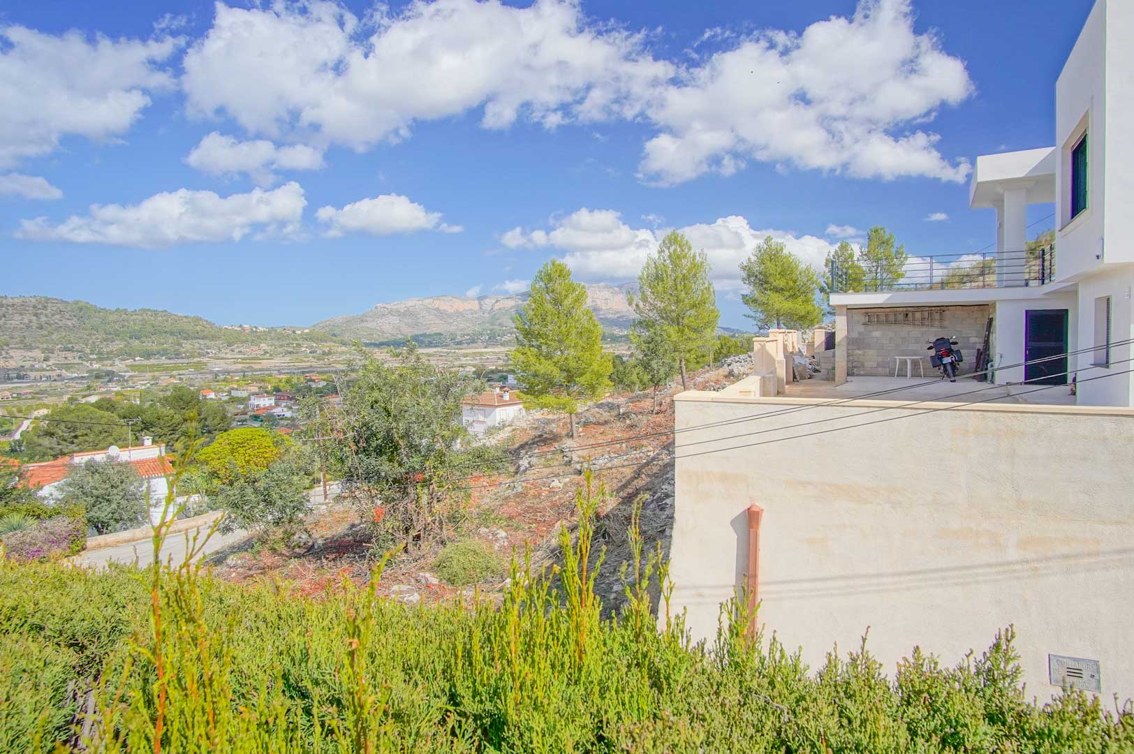 Vue extérieure de la terrasse et de la zone de stationnement de la villa, offrant un panorama dégagé sur la vallée et les montagnes.
