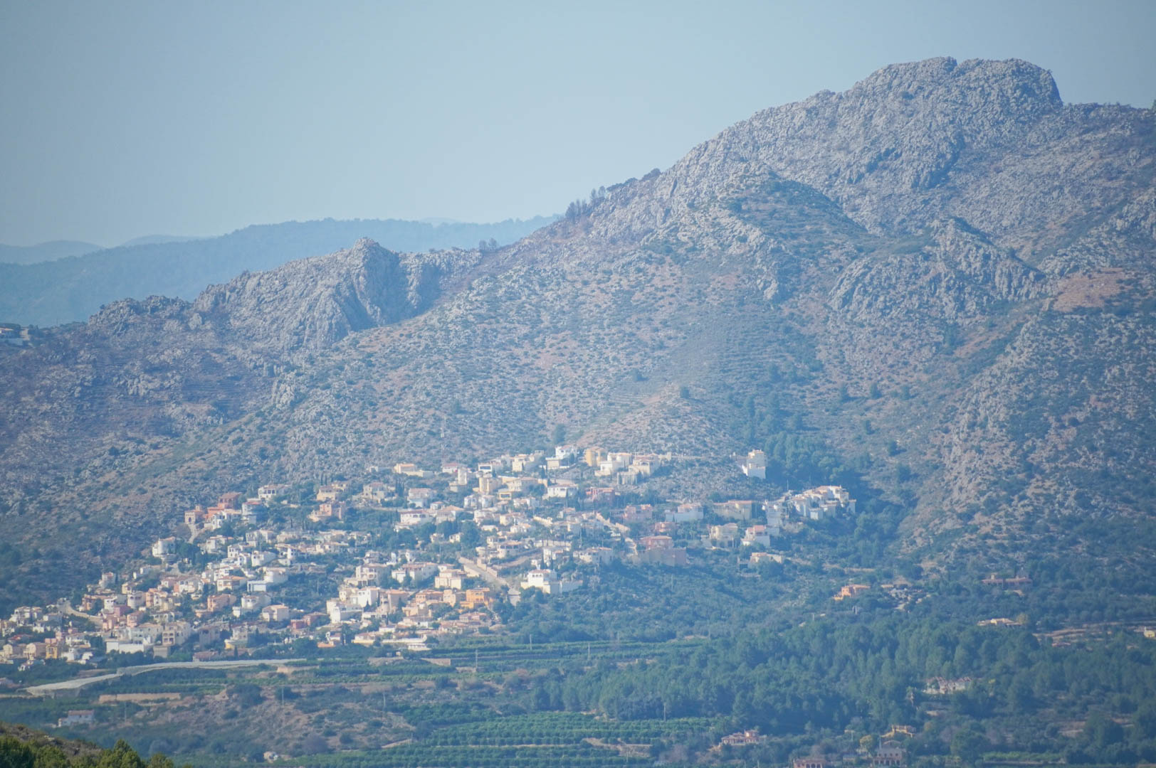 Vue panoramique sur les montagnes et la vallée, illustrant un quartier résidentiel niché à flanc de colline au-dessus de champs agricoles.