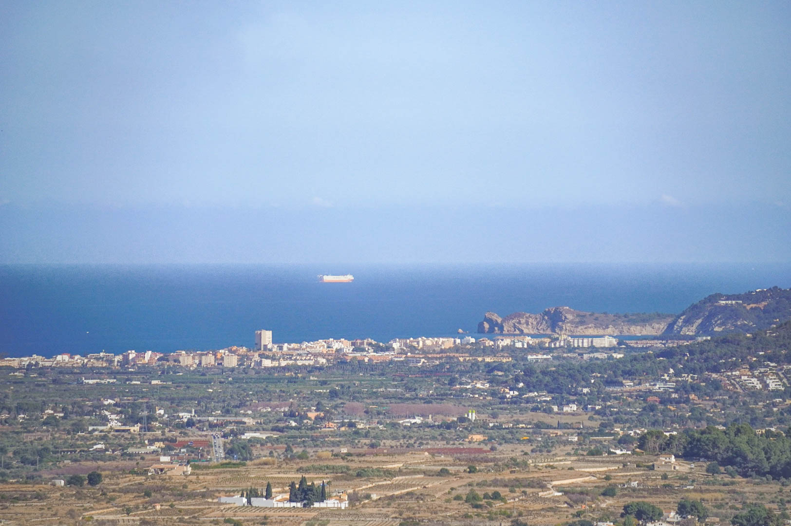 Vues panoramiques dégagées sur la côte méditerranéenne, révélant la silhouette de la ville côtière et la mer avec des navires à l'horizon.