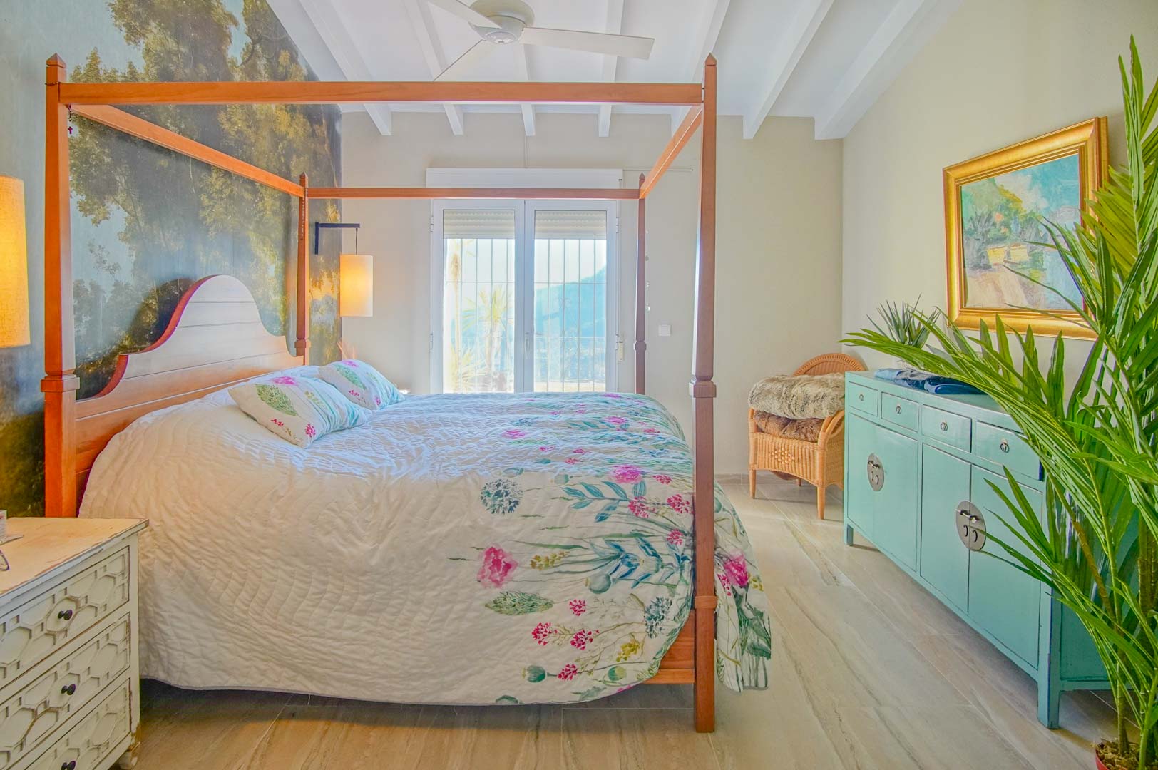 Chambre avec lit à baldaquin en bois, papier peint panoramique forestier, plafond à poutres blanches et accès direct vers l'extérieur.