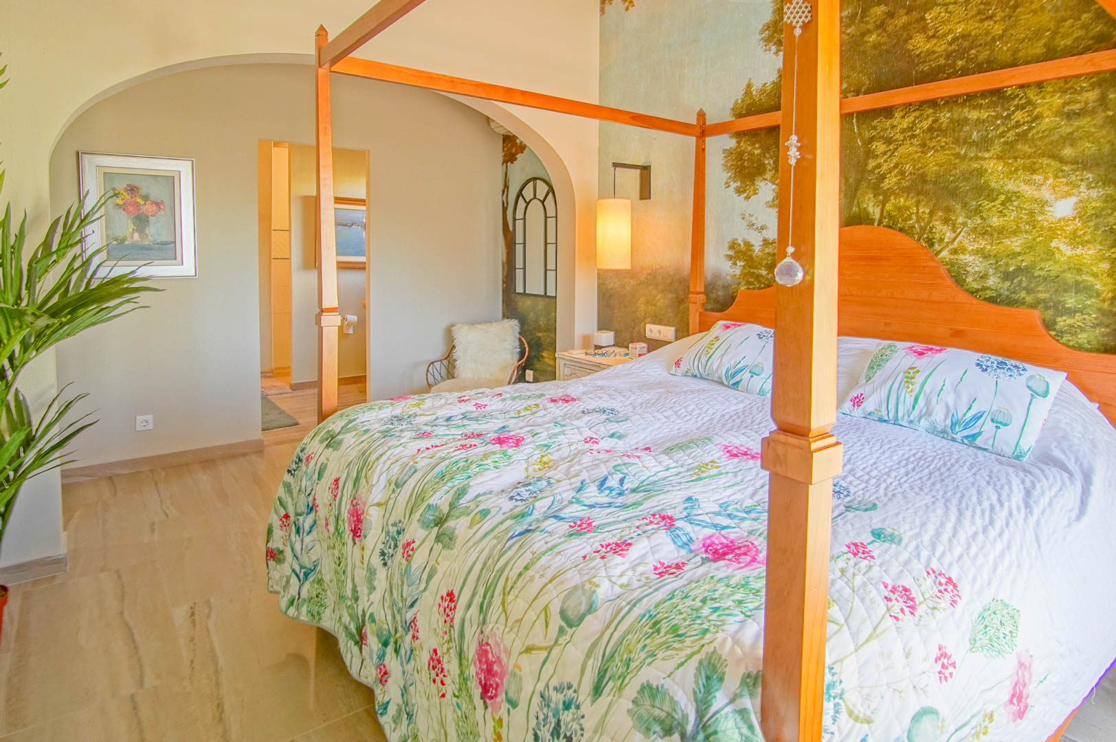 Chambre principale avec lit à baldaquin en bois, papier peint panoramique et sol en marbre. Une arche élégante mène directement à la salle de bain attenante.