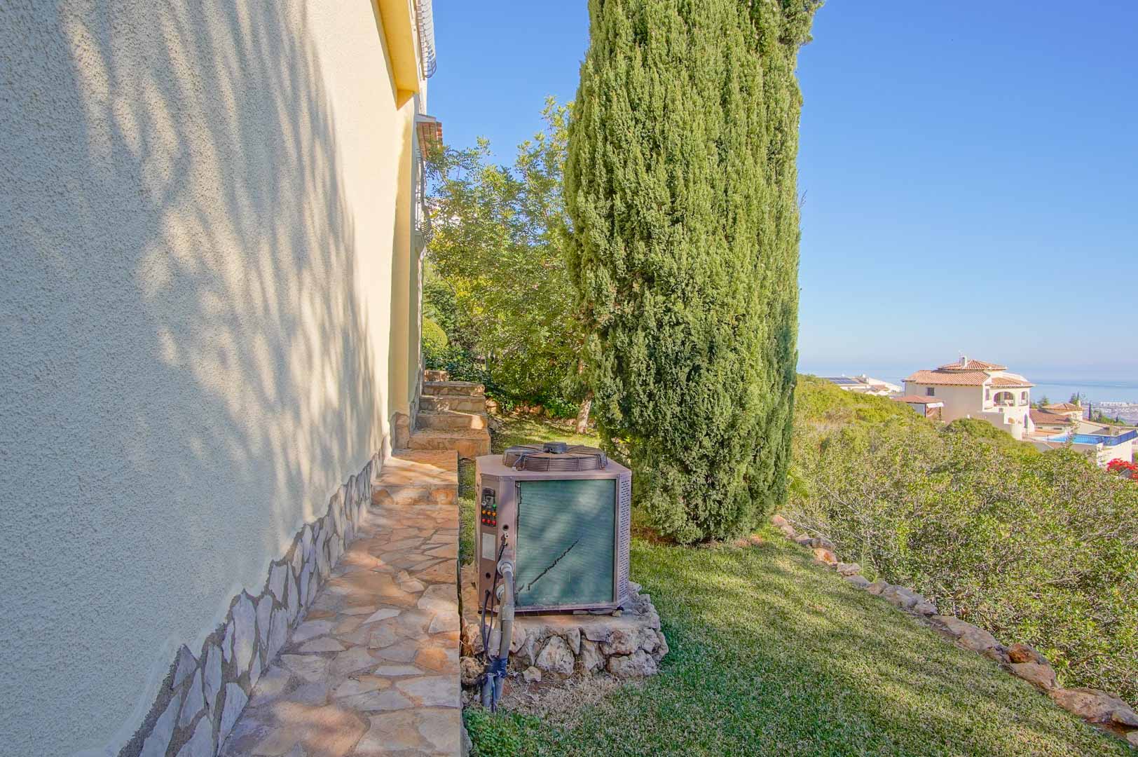 Chemin latéral en pierre naturelle bordant la façade, offrant une vue dégagée sur la mer et un jardin méditerranéen agrémenté d'un grand cyprès.
