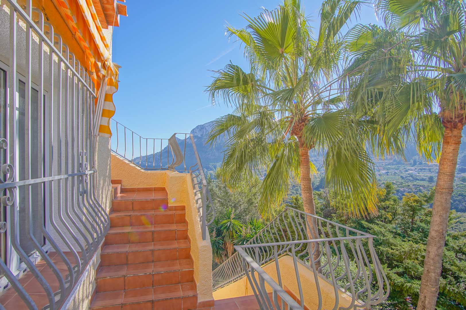 Escalier extérieur en terre cuite avec rampes en fer forgé, offrant une vue sur les montagnes et les palmiers du jardin méditerranéen.