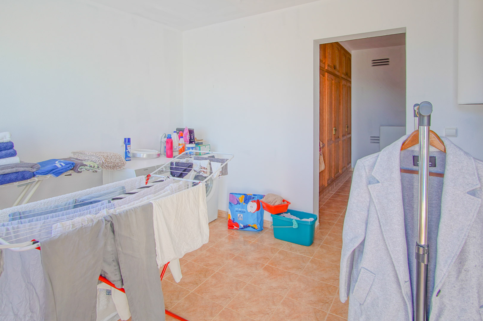 Espace buanderie pratique avec lave-linge et étendoirs, doté d'un sol en grès et d'un accès vers un couloir avec placards en bois intégrés.