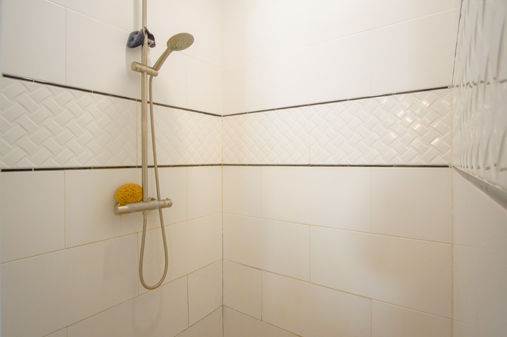 Espace douche avec carrelage mural blanc, frise décorative à relief tressé et robinetterie en acier inoxydable réglable.