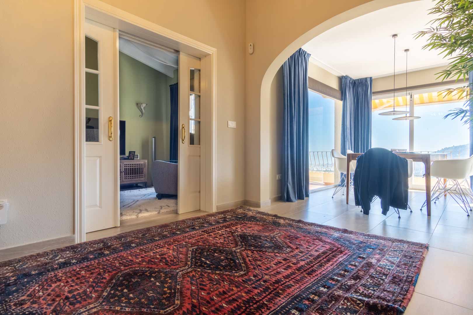 Hall d'entrée avec tapis d'orient, portes coulissantes vitrées menant au salon et arche ouvrant sur une salle à manger lumineuse face à la mer Méditerranée.