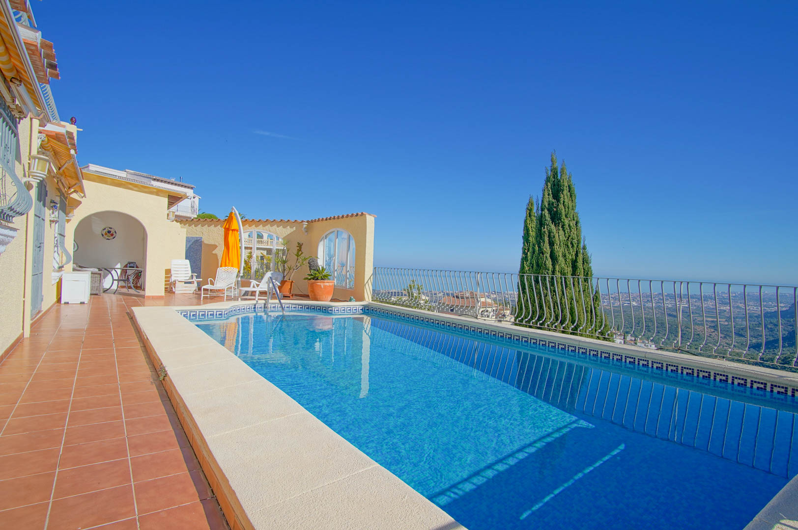 Piscine rectangulaire en mosaïque bleue avec frise grecque, terrasse en terre cuite et vue panoramique sur la Méditerranée et la vallée.