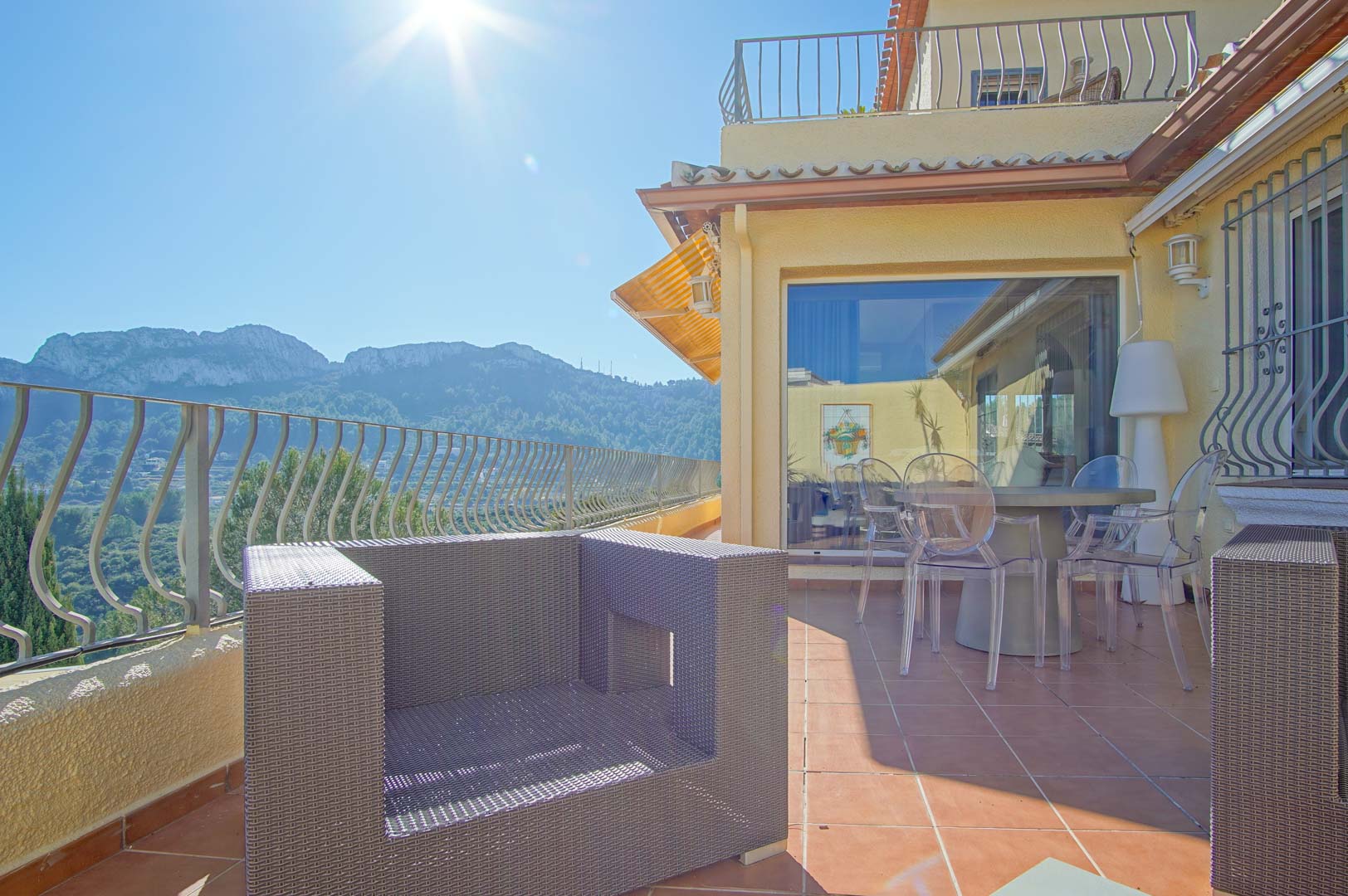 Terrasse avec carrelage en terre cuite, mobilier en rotin synthétique et chaises transparentes, offrant une vue panoramique sur les montagnes environnantes.
