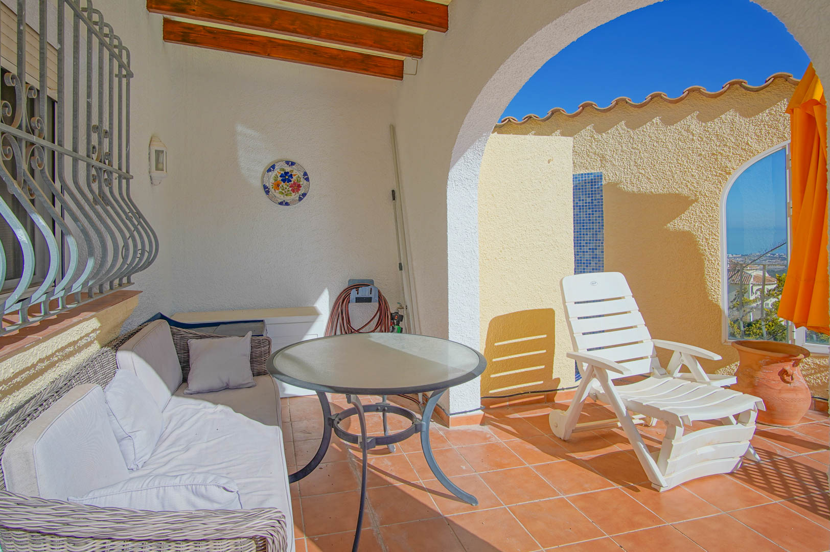 Terrasse couverte avec poutres apparentes, sol en terre cuite et salon extérieur menant à un solarium avec vue mer et douche en mosaïque.