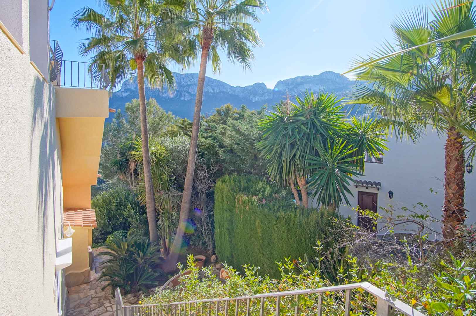 Vue depuis l'escalier extérieur sur le massif montagneux, encadrée par des palmiers et une végétation méditerranéenne dense et soignée.