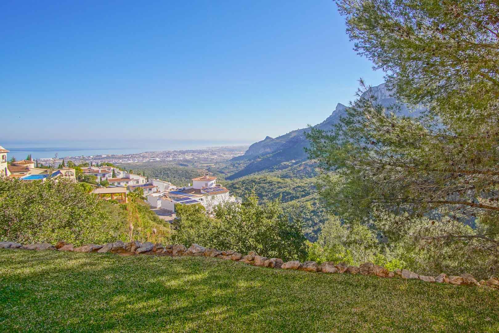 Vue panoramique depuis le jardin en pelouse sur la côte méditerranéenne et les crêtes montagneuses, entourée d'une végétation locale luxuriante.