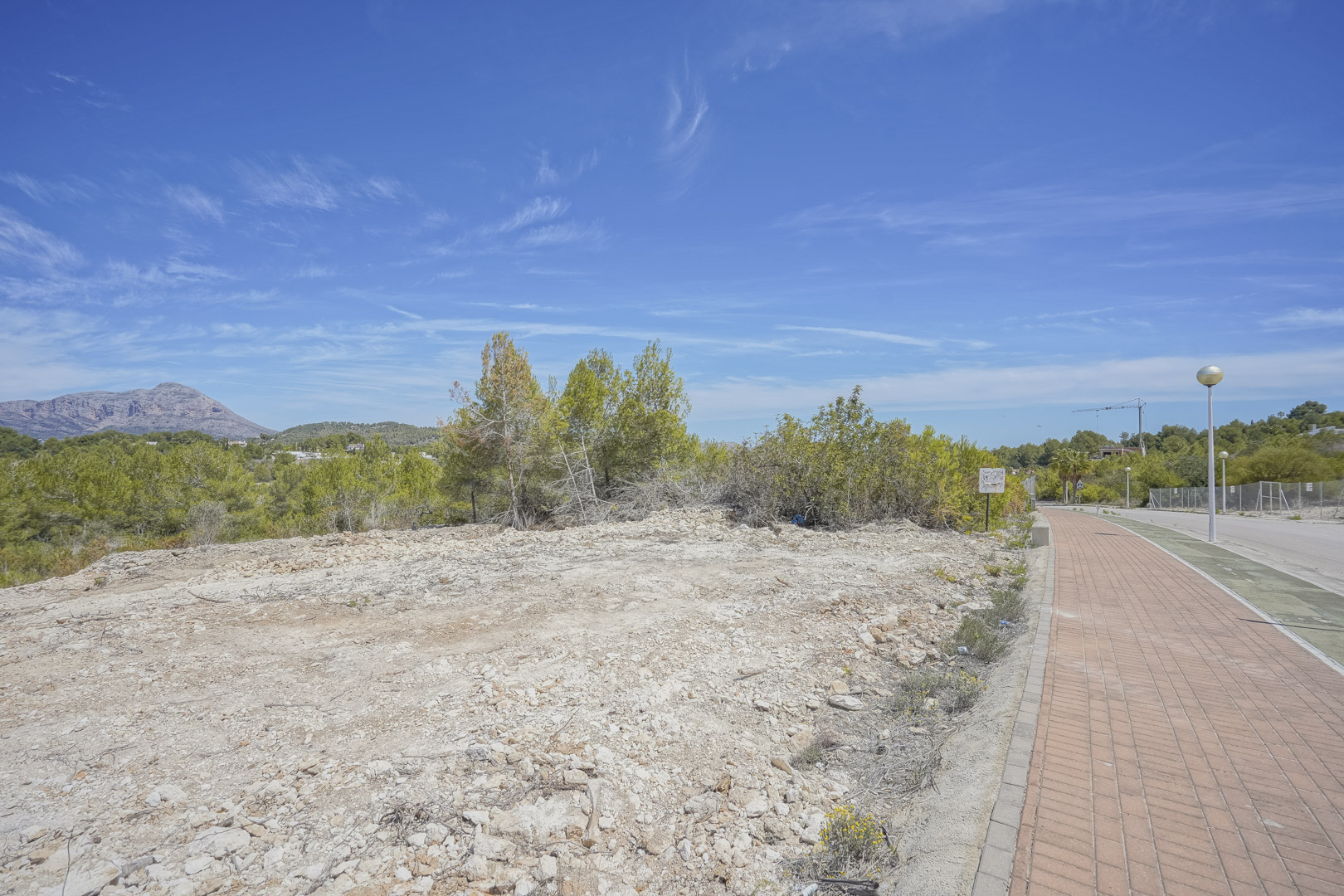 Terrain à bâtir de 1 000 m2 à Jávea, offrant une surface dégagée avec vue sur le Montgó, situé en bordure d'une zone résidentielle avec trottoirs pavés.