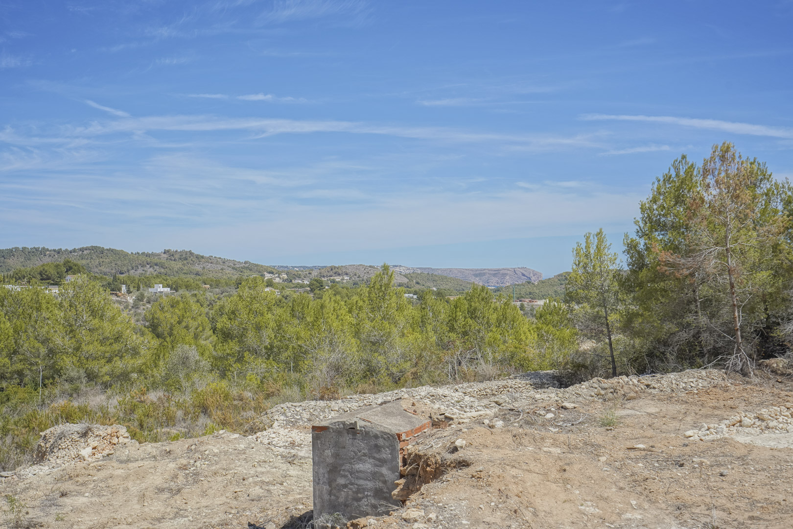 Vue panoramique depuis le terrain surélevé, mettant en valeur le paysage méditerranéen parsemé de pins et les montagnes de Jávea.