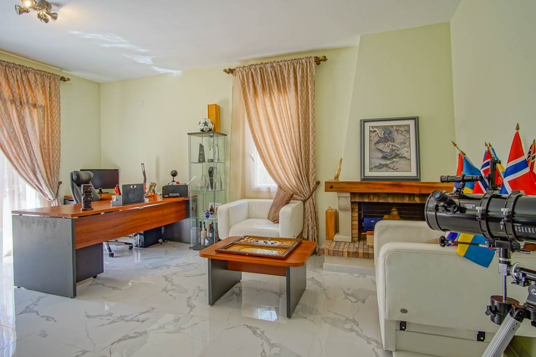 Bureau lumineux doté d'un sol effet marbre, d'un grand bureau en bois, d'une cheminée traditionnelle et d'un coin salon avec fauteuils en cuir blanc.