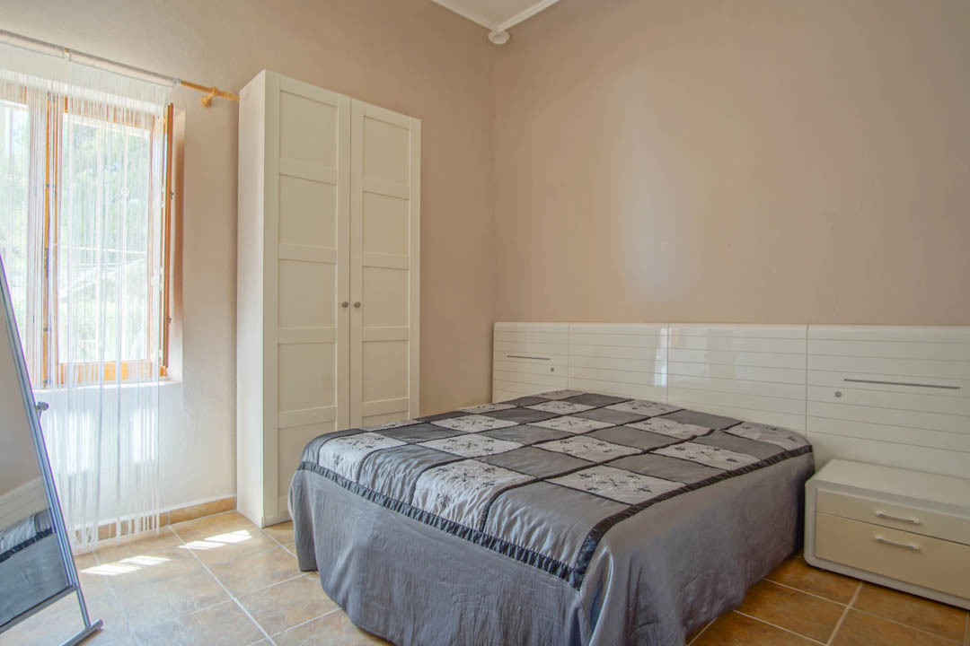 Chambre avec sol en carrelage, armoire blanche autoportante et tête de lit avec tables de chevet intégrées, éclairée par la lumière naturelle.