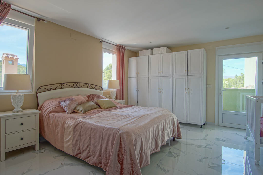 Chambre avec sol en grès cérame effet marbre, grandes armoires blanches et accès balcon offrant une vue sur les montagnes environnantes.