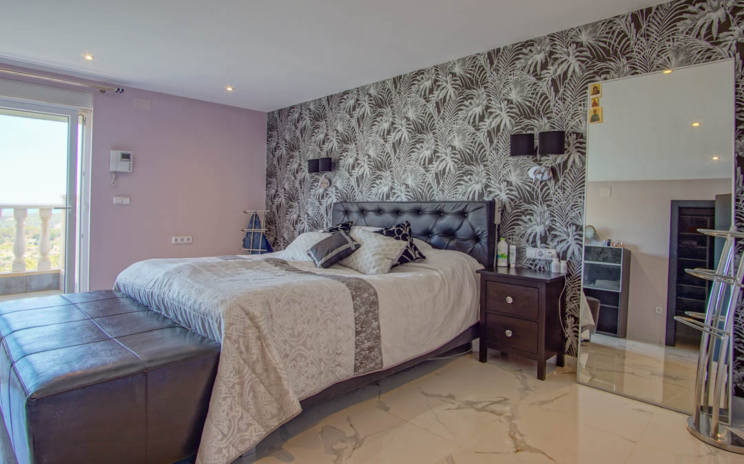 Chambre avec sol en marbre, mur d'accent au motif tropical, tête de lit en cuir capitonné et accès à un balcon avec balustrade.