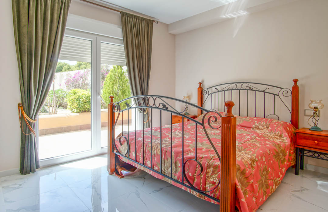 Chambre avec sol en marbre poli, lit en fer forgé et bois, et accès direct à la terrasse par de grandes baies vitrées offrant une lumière naturelle.