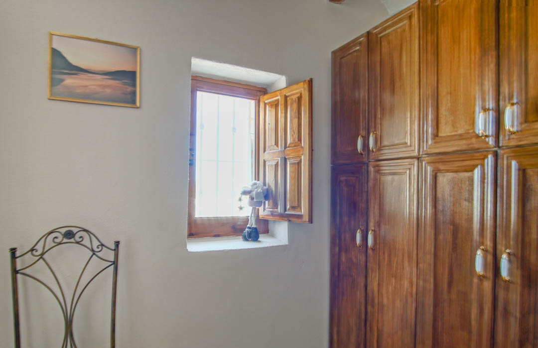Chambre rustique avec armoire encastrée en bois massif, fenêtre traditionnelle à volets en bois et chaise décorative en fer forgé.
