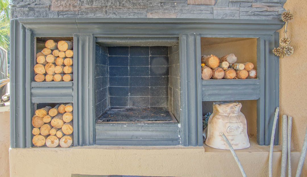 Cheminée extérieure intégrée avec barbecue central, parement en pierre et niches latérales pour le stockage du bois de chauffage.