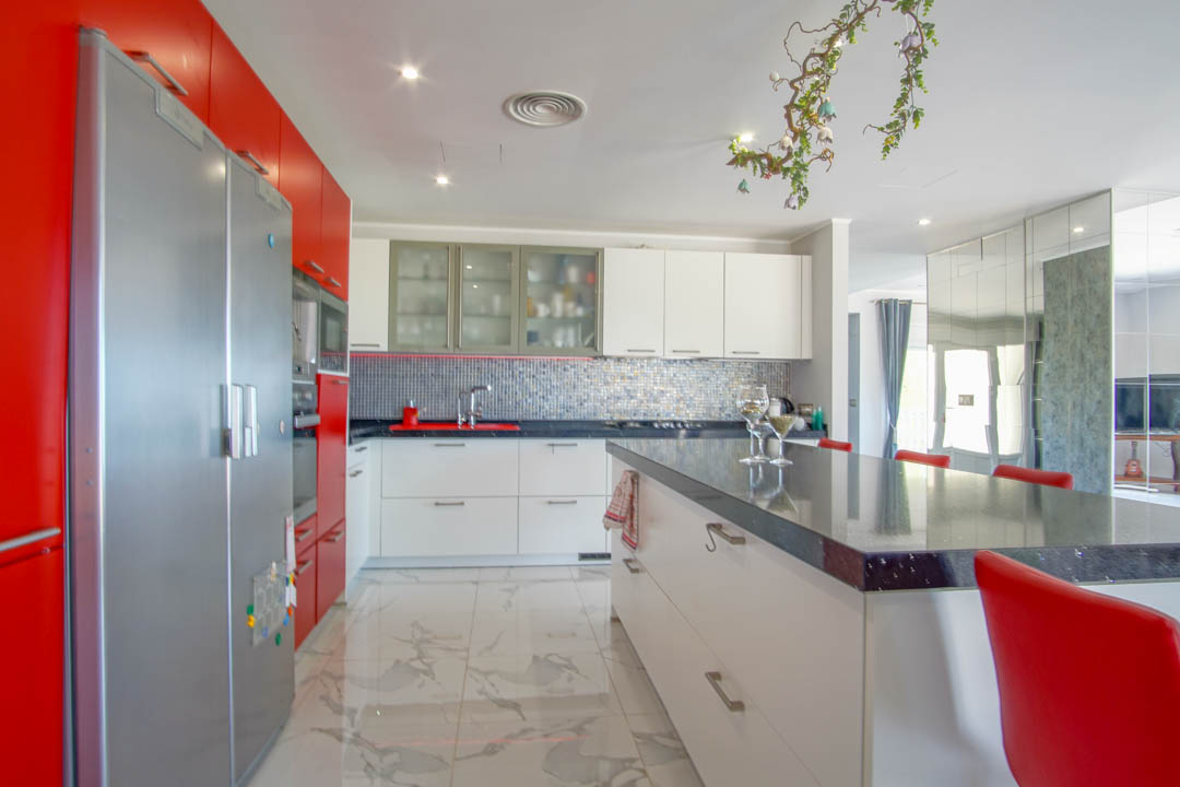 Cuisine contemporaine avec des finitions rouges et blanches, un îlot central généreux et un sol élégant en grès cérame à l'aspect marbré.