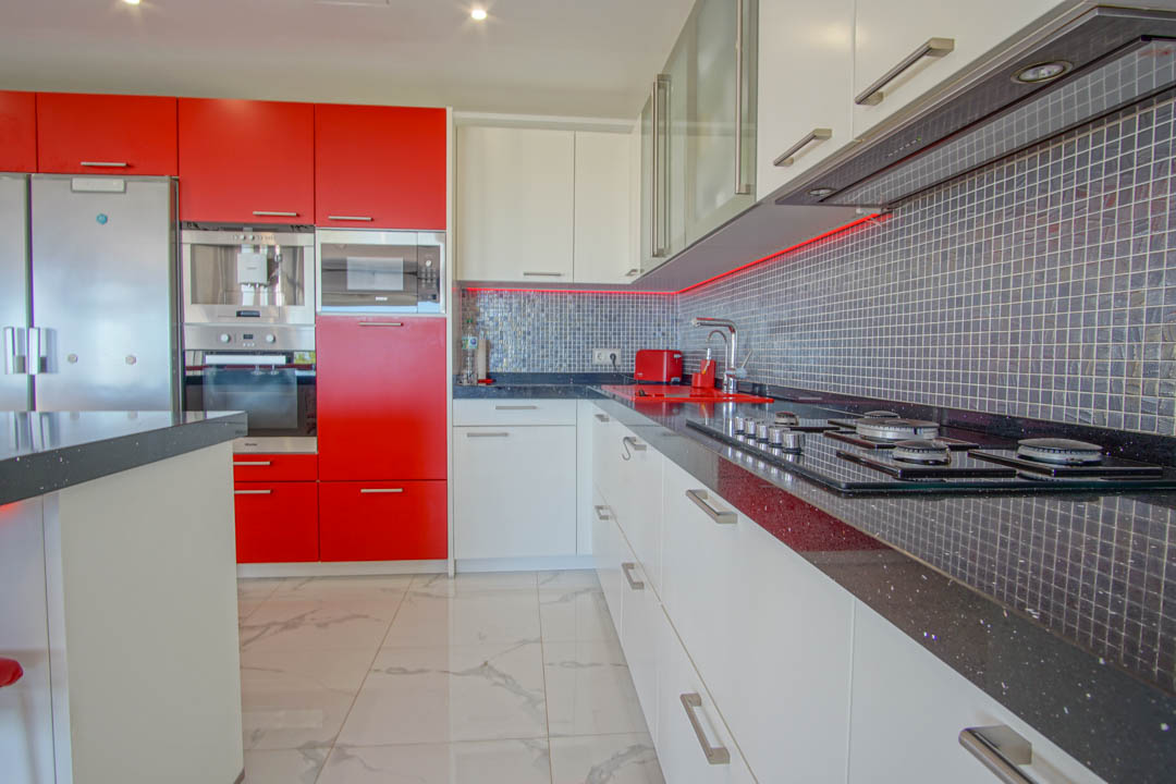 Cuisine moderne avec armoires laquées rouges et blanches, plans de travail en granit noir et crédence en mosaïque grise avec éclairage LED.
