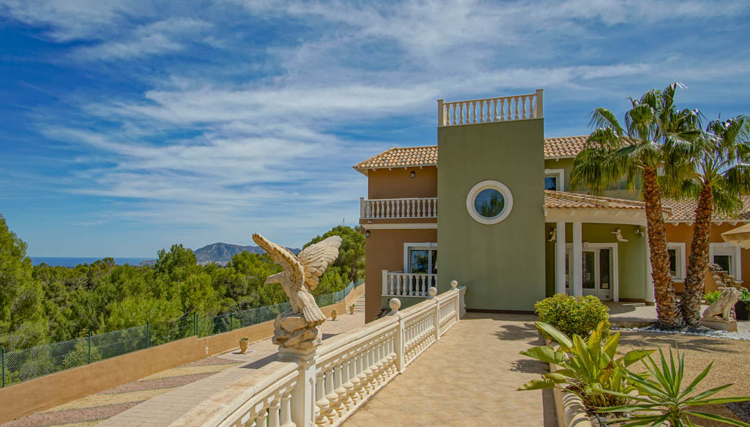 Façade extérieure avec balustrades classiques, sculpture d'aigle ornementale et entrée bordée de palmiers offrant une vue panoramique sur la pinède et la mer Méditerranée.