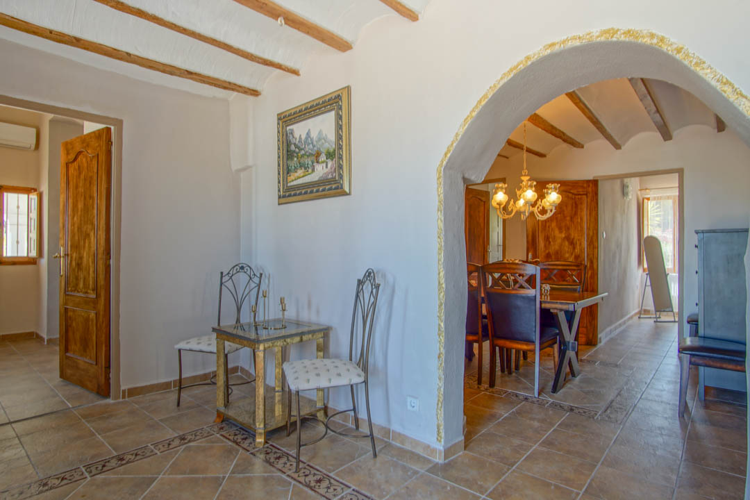 Hall d'entrée avec poutres en bois apparentes et sol en grès, s'ouvrant sur la salle à manger par une arche aux finitions texturées dorées.