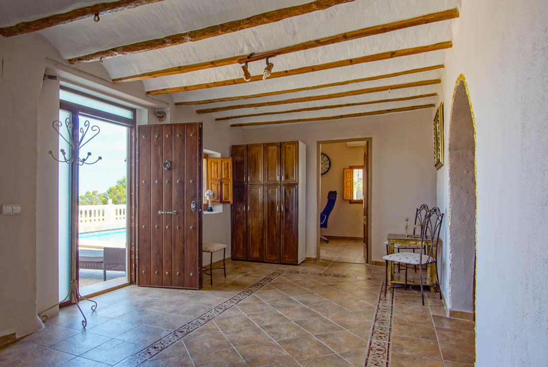 Hall d'entrée rustique avec poutres en bois apparentes, sol en carrelage décoré et une porte massive en bois clouté s'ouvrant sur la terrasse de la piscine.