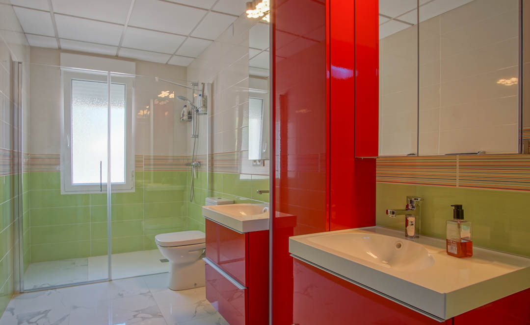Salle de bain contemporaine avec meuble vasque rouge laqué, douche à l'italienne vitrée et carrelage mural bicolore vert et blanc.
