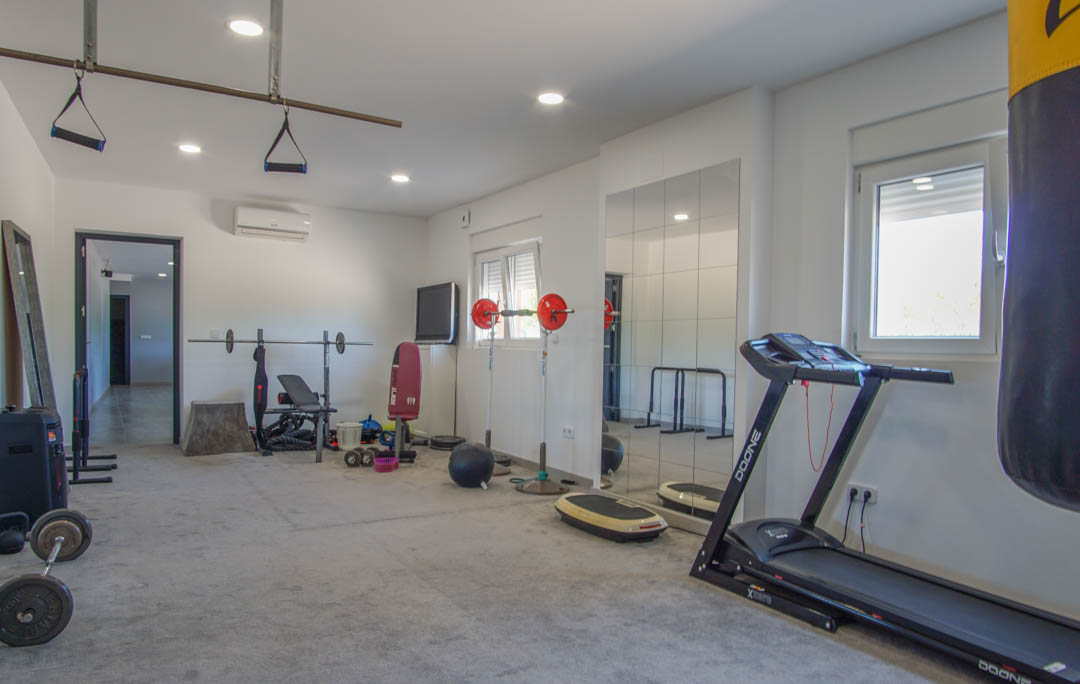 Salle de sport privée équipée d'un tapis de course, d'un sac de frappe et d'haltères. Espace climatisé avec miroirs muraux et éclairage encastré.