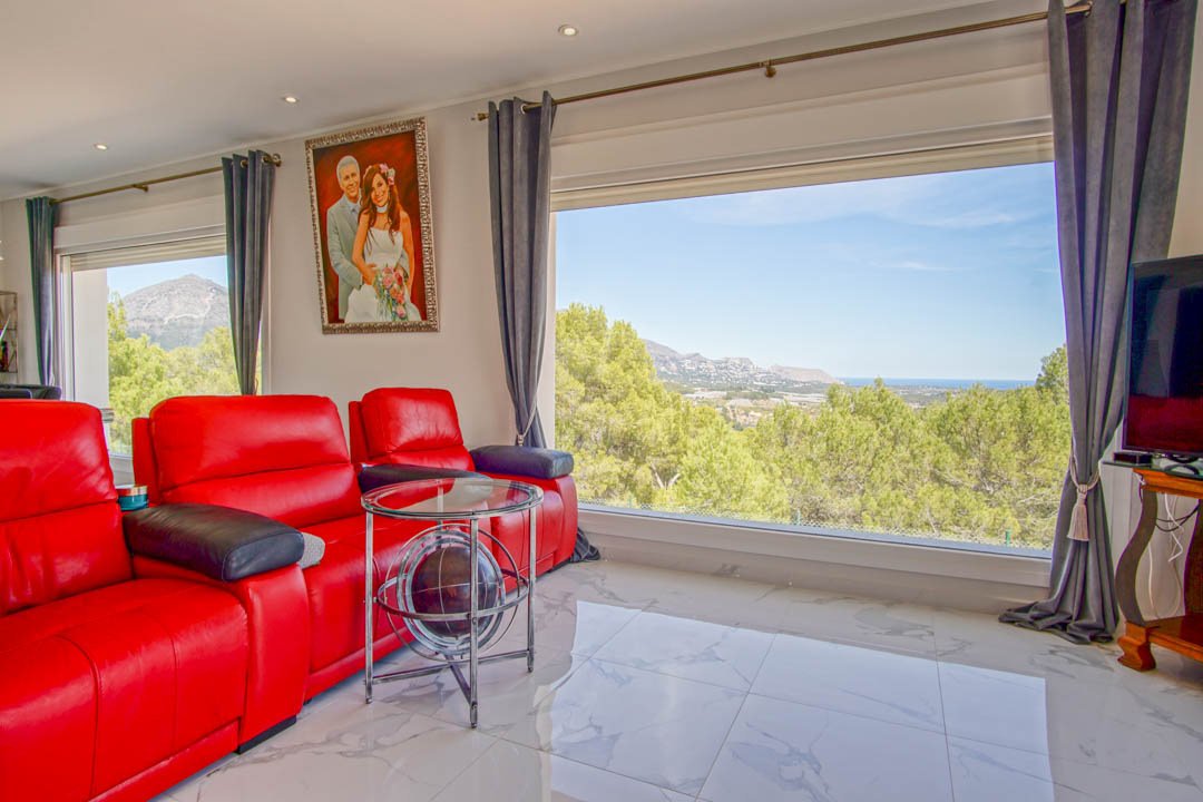Salon lumineux avec fauteuils en cuir rouge, sol en marbre blanc et grandes fenêtres offrant une vue panoramique sur la mer Méditerranée et les montagnes.