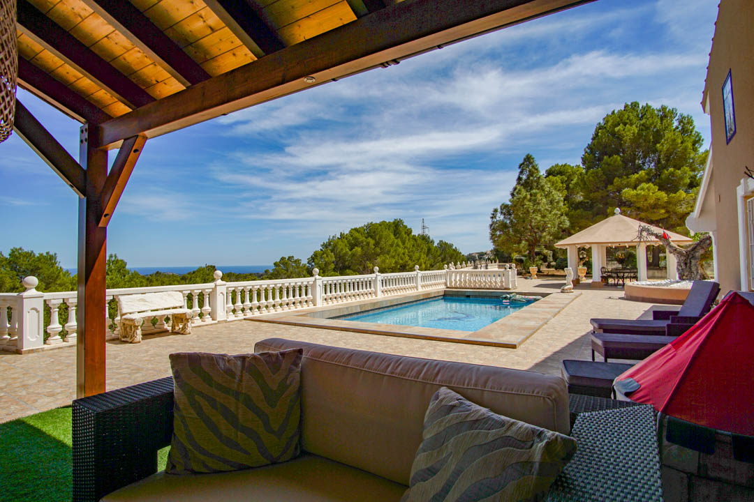 Terrasse avec piscine, balustrade blanche et vue panoramique sur la mer. Comprend un salon sous pergola en bois et un pavillon entouré de pins méditerranéens.