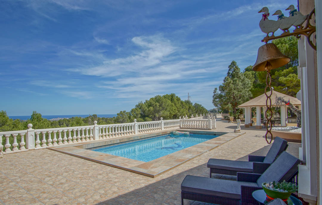 Terrasse avec piscine en mosaïque et balustrade blanche, offrant une vue dégagée sur la côte méditerranéenne et les pinèdes.