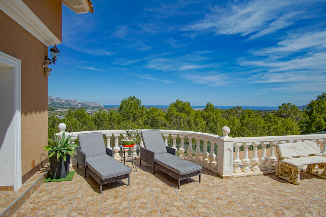 Terrasse surélevée avec sol en pierre, balustrade blanche et chaises longues grises, offrant une vue panoramique sur la forêt de pins et la mer Méditerranée.