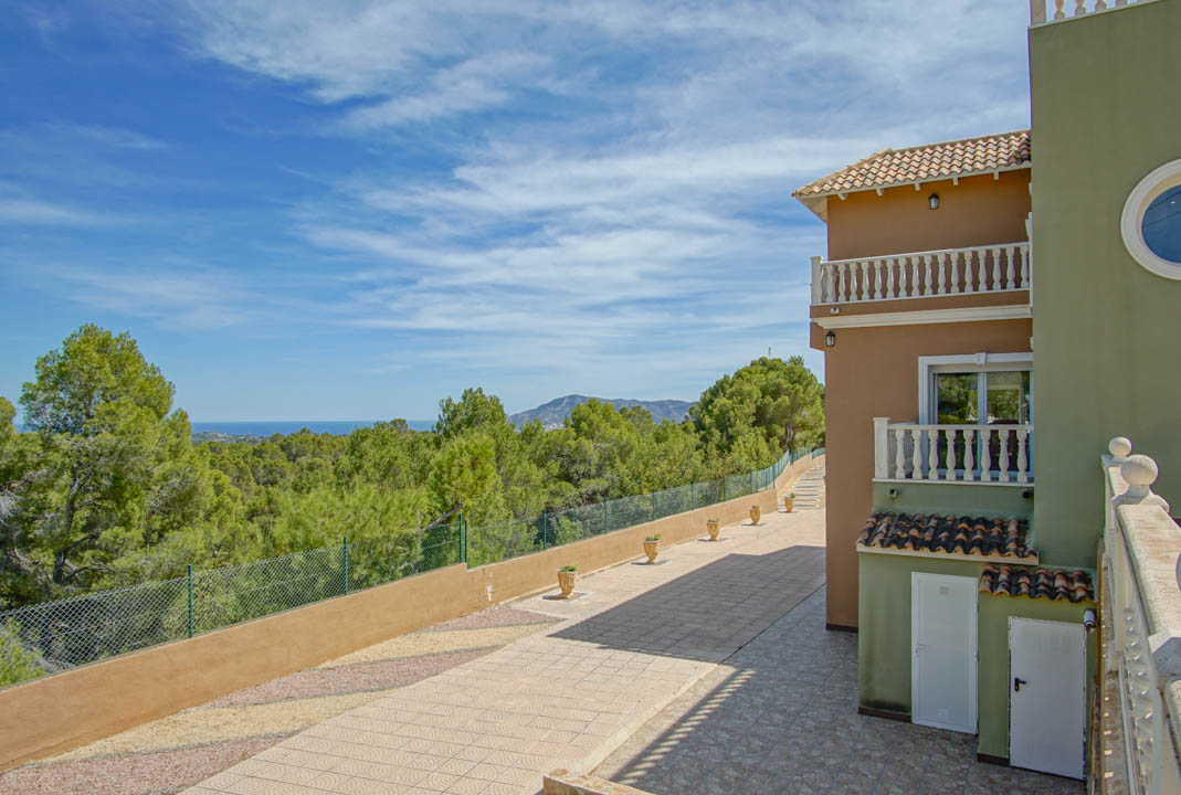 Vue extérieure de la façade avec balcons à balustrades, chemin pavé et vue panoramique sur la pinède environnante s'étendant jusqu'à la mer Méditerranée.