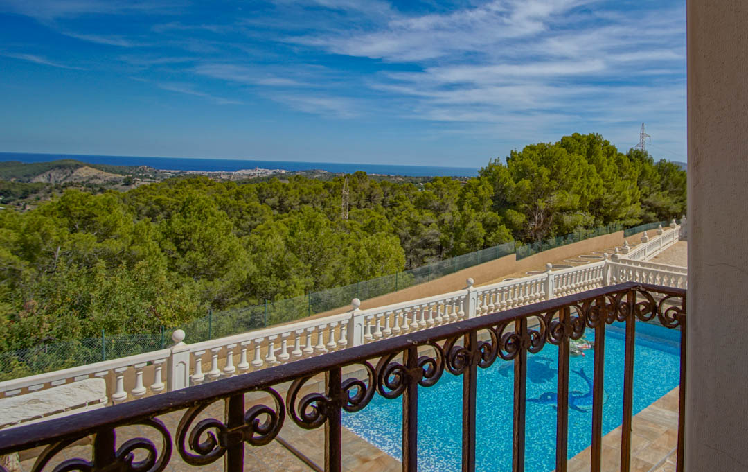 Vue surélevée depuis un balcon en fer forgé, dominant la piscine et une forêt de pins avec un panorama dégagé sur la mer Méditerranée.