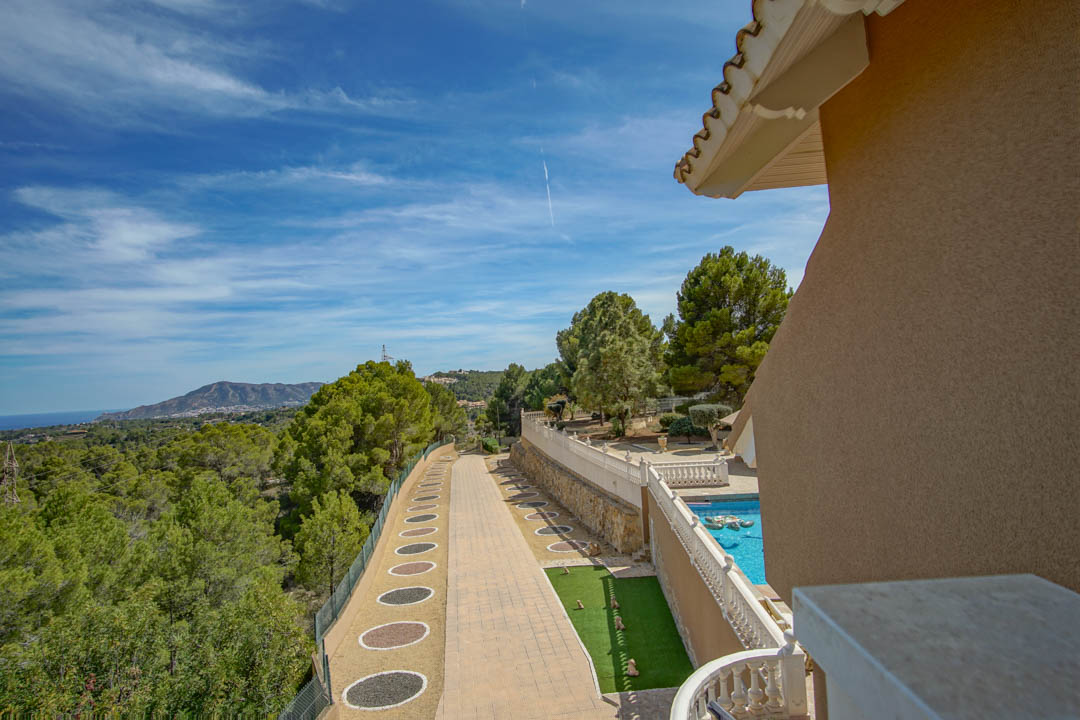 Vue surélevée sur l'allée pavée, l'espace piscine bordé d'une balustrade blanche et le paysage environnant offrant une vue dégagée sur la mer et les montagnes.