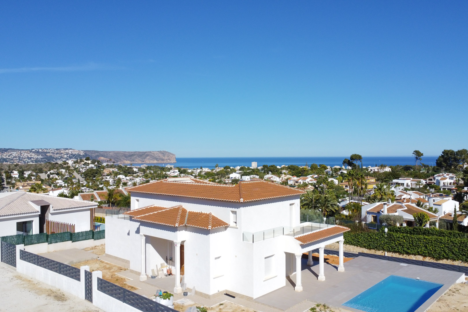 Vue aérienne de la villa blanche avec toiture en tuiles, piscine rectangulaire et terrasses à balustrades en verre offrant une vue panoramique sur la mer Méditerranée.