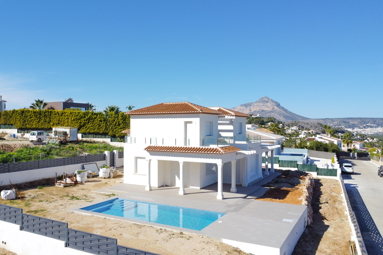 Vue aérienne de la villa soulignant la piscine rectangulaire, la grande terrasse carrelée et la silhouette du Montgó en arrière-plan sous un ciel dégagé.