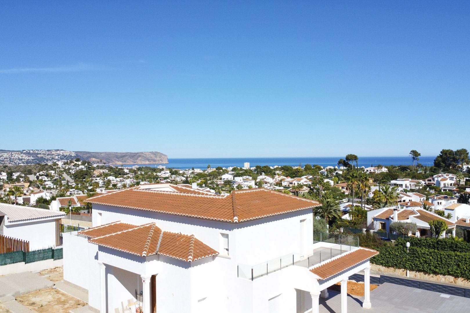 Vue extérieure de la villa aux façades blanches et toits en tuiles, incluant des terrasses avec garde-corps en verre et un panorama sur la mer Méditerranée.