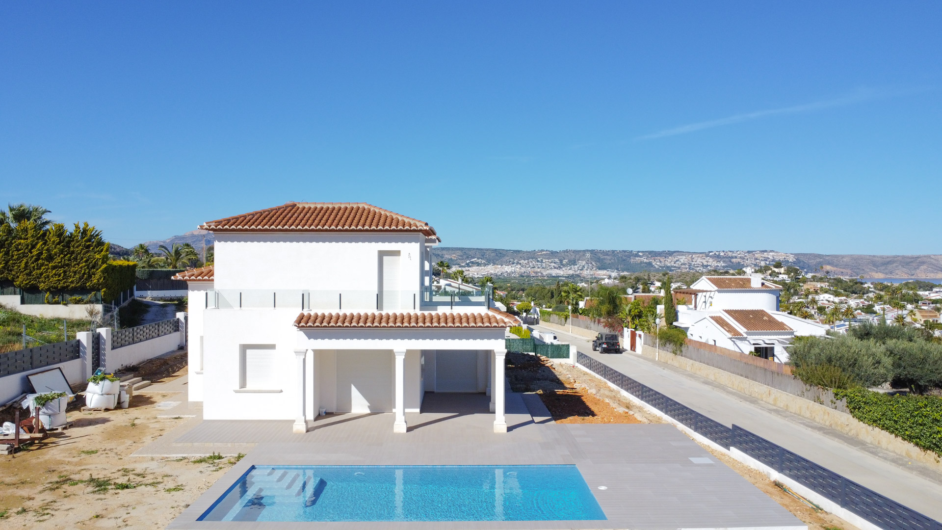 Vue extérieure de la villa avec sa piscine rectangulaire, sa façade blanche à deux niveaux et ses terrasses supérieures dotées de garde-corps en verre.