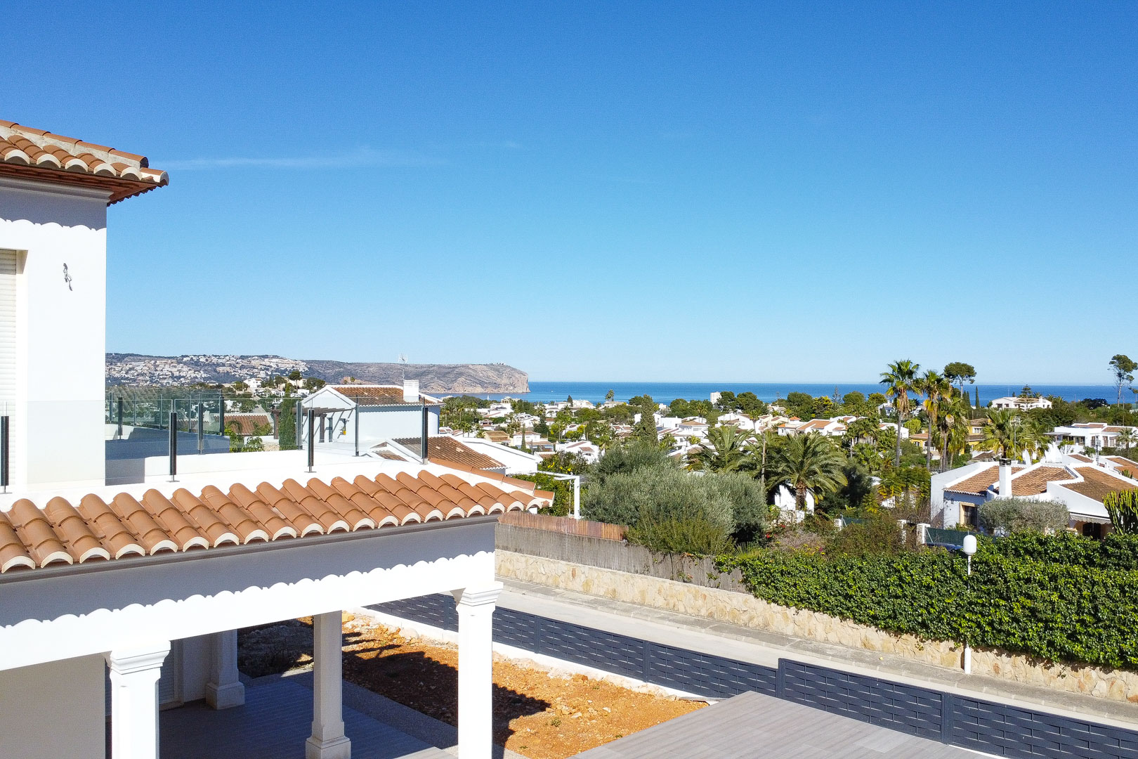 Vue panoramique sur la mer Méditerranée depuis la terrasse supérieure, mettant en valeur l'architecture blanche, les tuiles romanes et les garde-corps en verre.