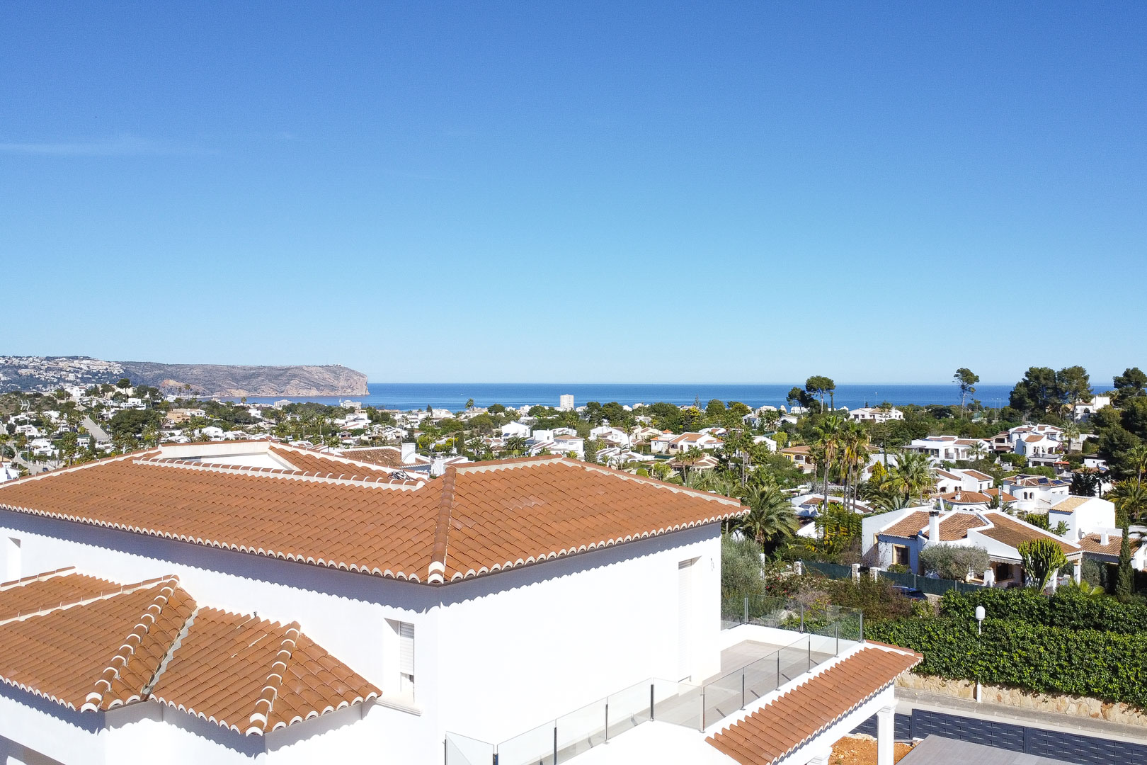Vue surélevée révélant la toiture en tuiles, la terrasse avec garde-corps en verre et un panorama dégagé sur la mer Méditerranée et les falaises environnantes.