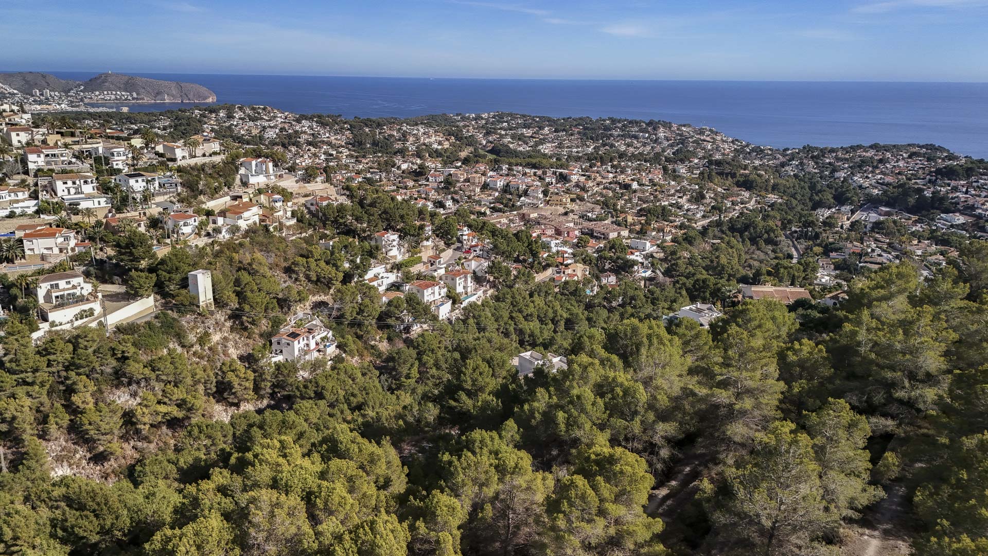 Vue aérienne illustrant l'intégration résidentielle dans le paysage naturel de Benissa, avec ses forêts de pins denses et sa vue panoramique sur la mer Méditerranée.