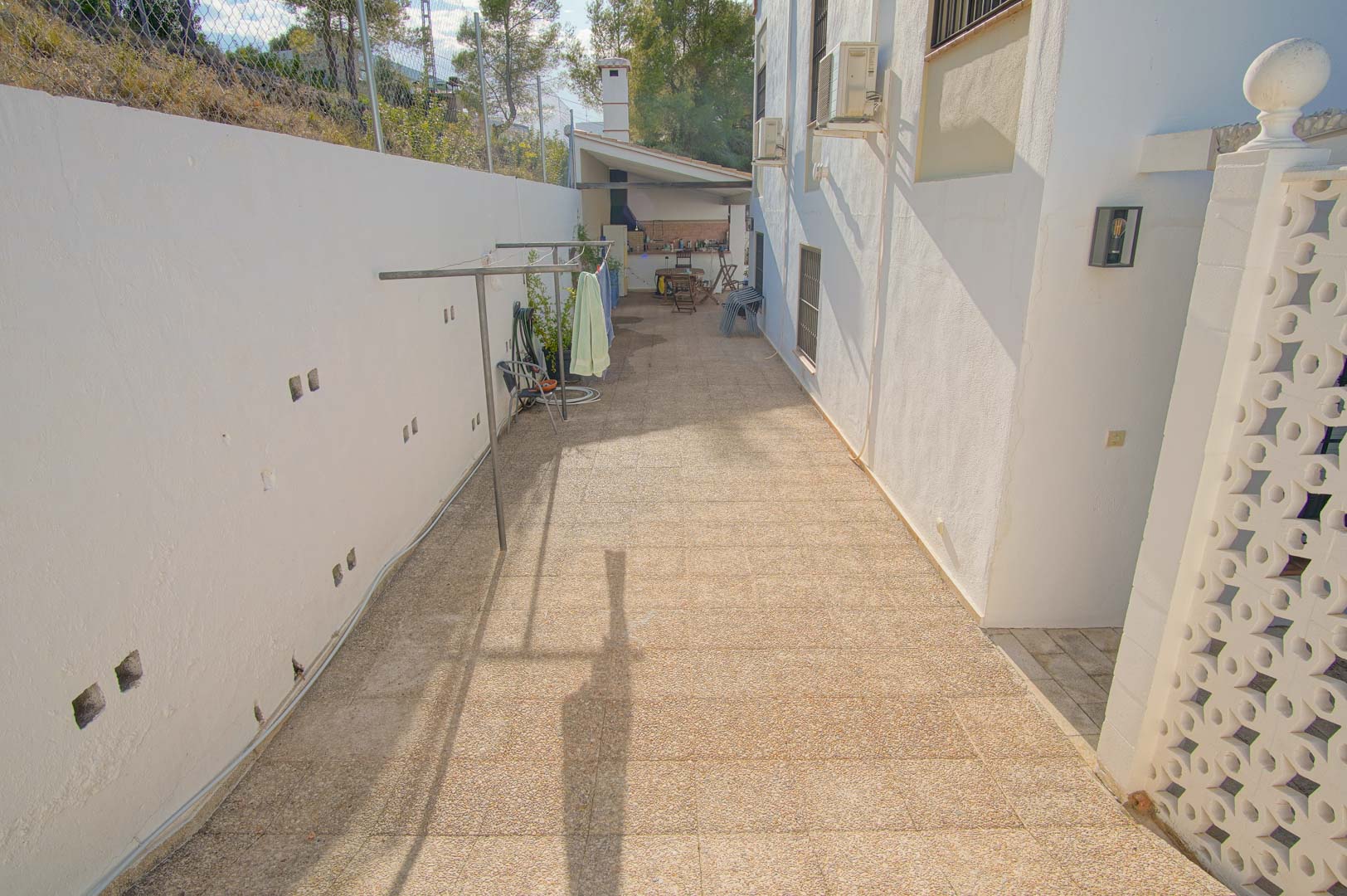 Allée latérale pavée avec espace buanderie extérieur, menant vers la cuisine d'été et la zone de barbecue couverte.